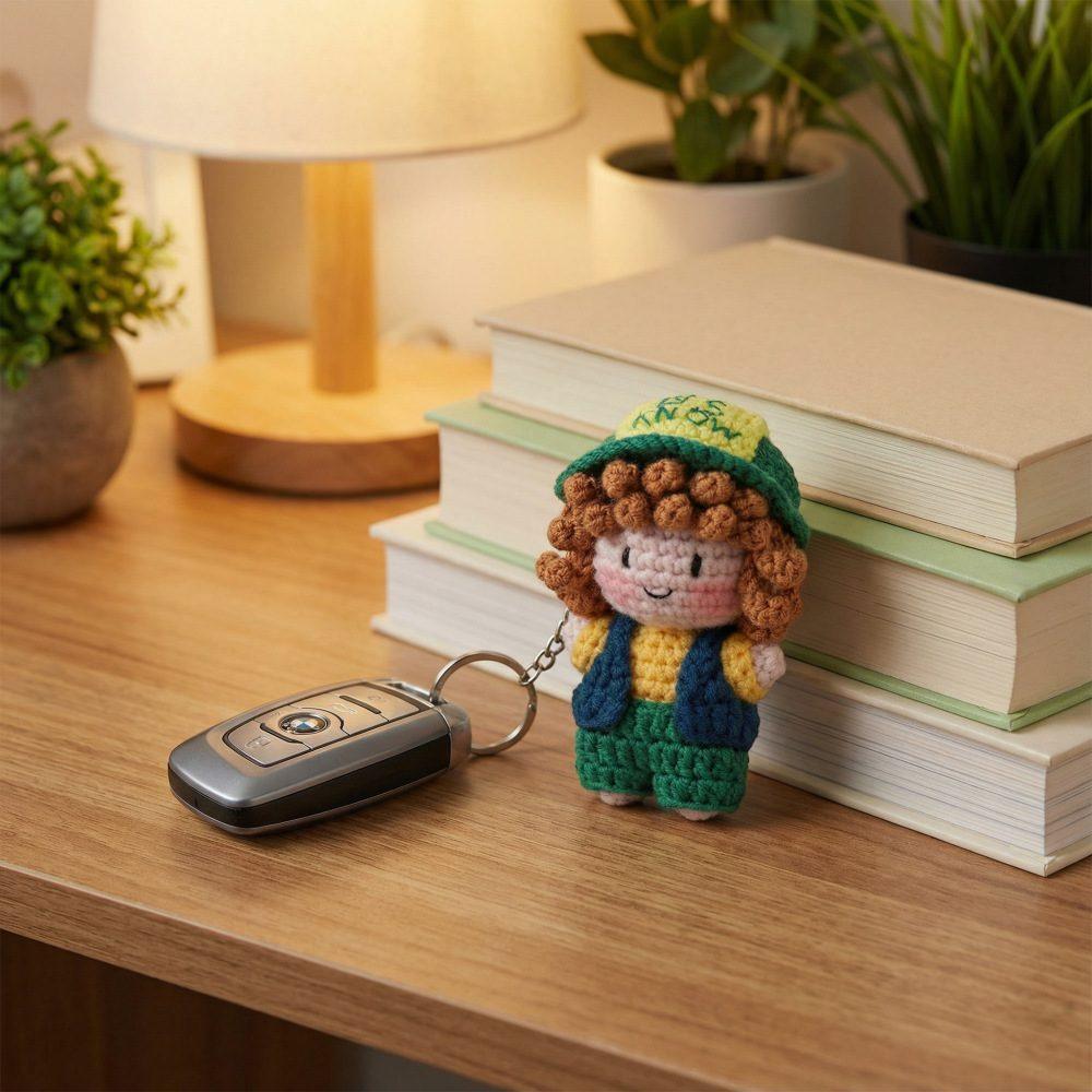 Small handmade crochet girl keychain wearing a green hat and navy jacket